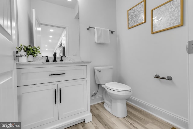 bathroom featuring baseboards, wood finished floors, toilet, and vanity