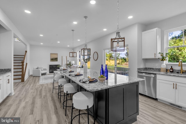 kitchen with sink, white cabinetry, a kitchen island, light hardwood / wood-style flooring, and stainless steel dishwasher