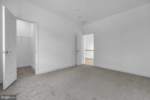 unfurnished bedroom with a closet, baseboards, carpet flooring, and a walk in closet