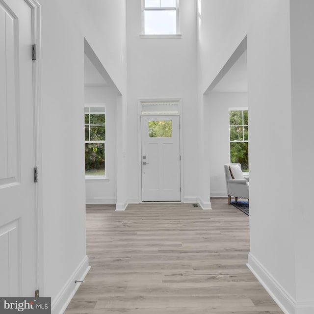 entryway with a towering ceiling, light wood-style floors, and baseboards