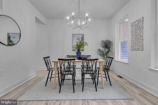 dining area with light wood-type flooring and an inviting chandelier