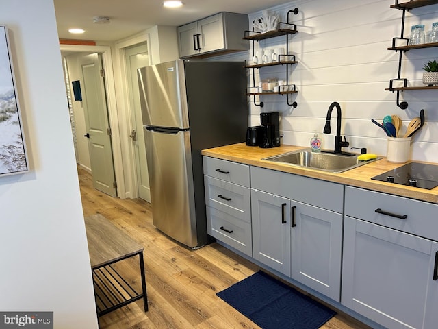 kitchen with light hardwood / wood-style floors, stainless steel fridge, black electric cooktop, sink, and butcher block countertops