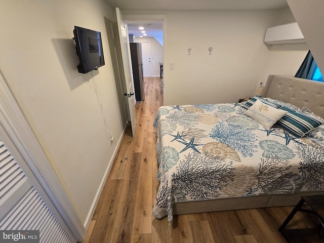 bedroom with wood-type flooring, stainless steel fridge, and a wall unit AC