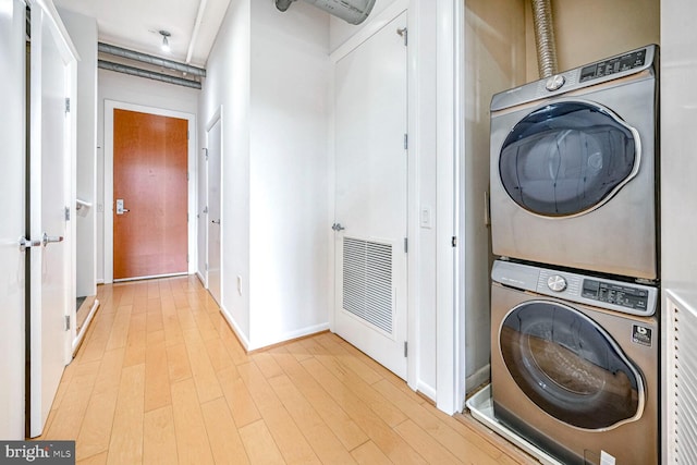 laundry room with light wood-type flooring and stacked washer and clothes dryer