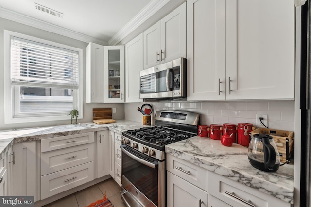 kitchen with white cabinets, light tile patterned flooring, stainless steel appliances, light stone countertops, and crown molding