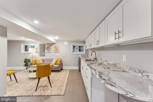 kitchen with light stone counters, white cabinets, electric panel, and sink