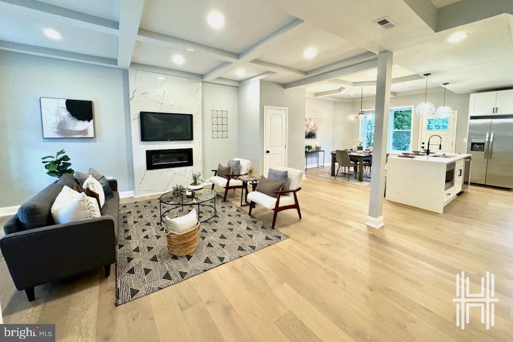 living room with coffered ceiling, beam ceiling, sink, light wood-type flooring, and a fireplace