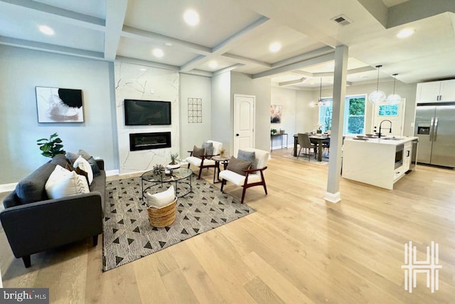 living room with coffered ceiling, beam ceiling, sink, light wood-type flooring, and a fireplace