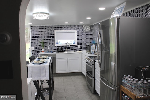 kitchen with appliances with stainless steel finishes, sink, backsplash, white cabinets, and light tile patterned floors