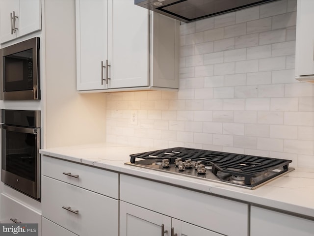 kitchen featuring light stone countertops, stainless steel appliances, tasteful backsplash, and white cabinetry