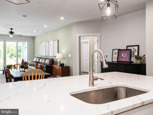 kitchen with light stone counters, ceiling fan, hanging light fixtures, and sink