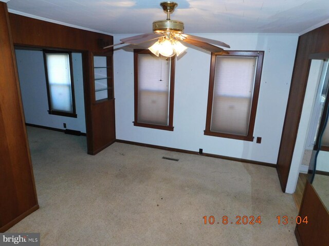 spare room with ceiling fan, light colored carpet, wood walls, and ornamental molding