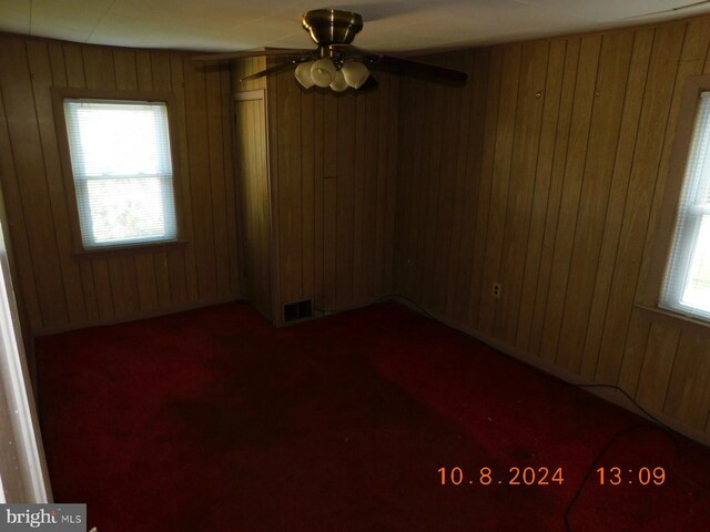 carpeted spare room featuring ceiling fan, wood walls, and a wealth of natural light