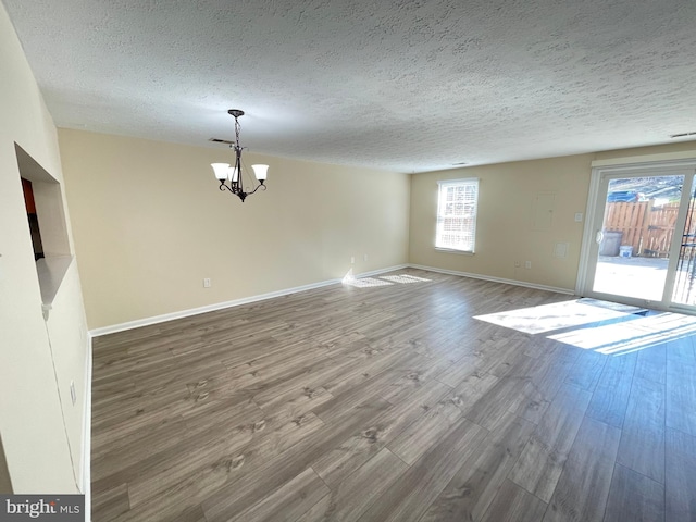 empty room with a textured ceiling, a notable chandelier, and hardwood / wood-style flooring