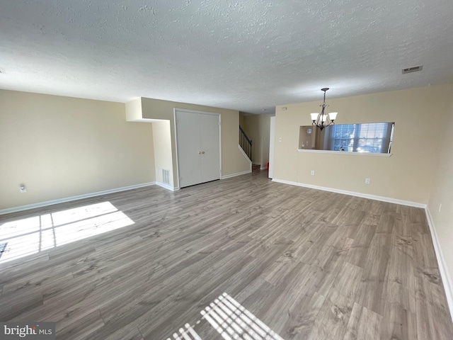 unfurnished living room with hardwood / wood-style flooring, a notable chandelier, and a textured ceiling