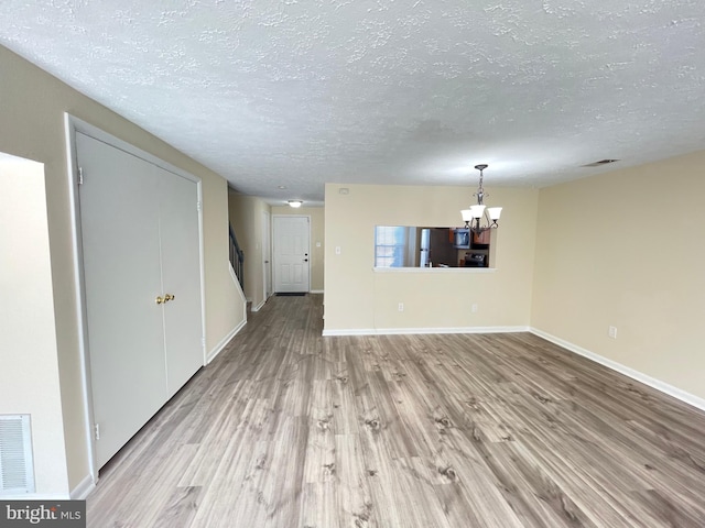 unfurnished living room with a textured ceiling, light wood-type flooring, and a chandelier