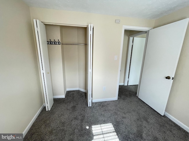 unfurnished bedroom featuring a textured ceiling, dark carpet, and a closet