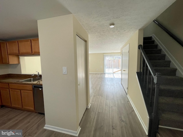 interior space with a textured ceiling, stainless steel dishwasher, hardwood / wood-style floors, and sink