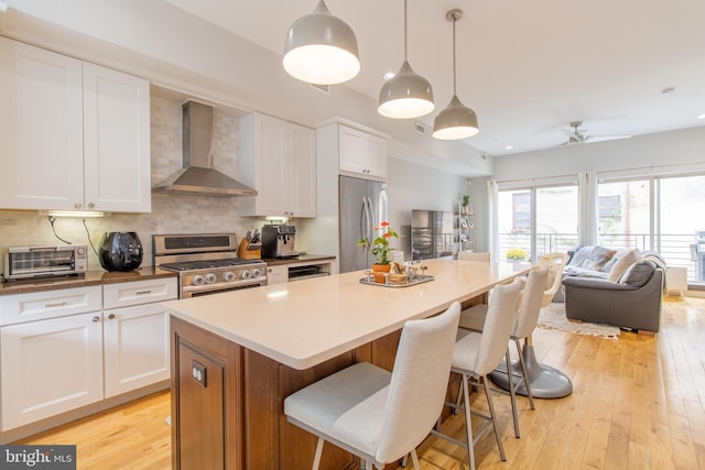 kitchen featuring white cabinets, appliances with stainless steel finishes, wall chimney exhaust hood, and light hardwood / wood-style floors