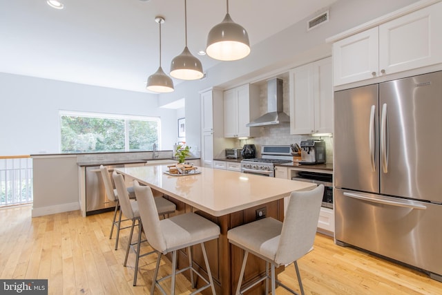 kitchen featuring wall chimney range hood, a kitchen island, light hardwood / wood-style flooring, appliances with stainless steel finishes, and white cabinetry