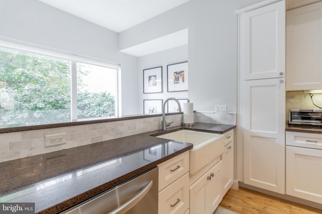 kitchen featuring dark stone countertops, sink, light hardwood / wood-style floors, white cabinetry, and backsplash