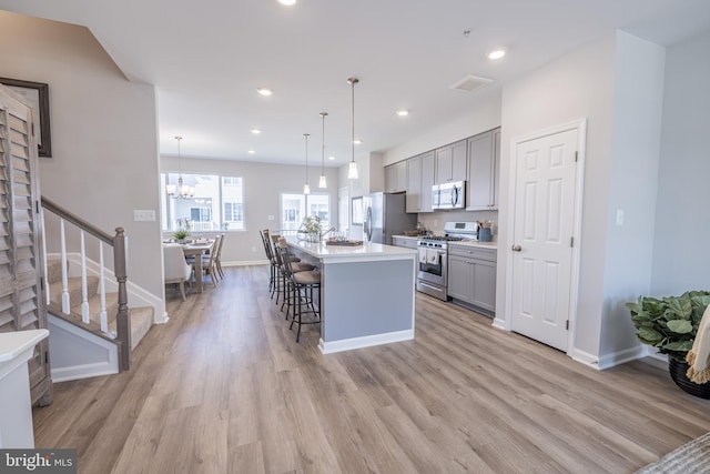 kitchen featuring a center island with sink, pendant lighting, light wood-type flooring, gray cabinets, and appliances with stainless steel finishes