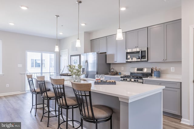 kitchen with gray cabinetry, stainless steel appliances, light hardwood / wood-style flooring, and a center island with sink