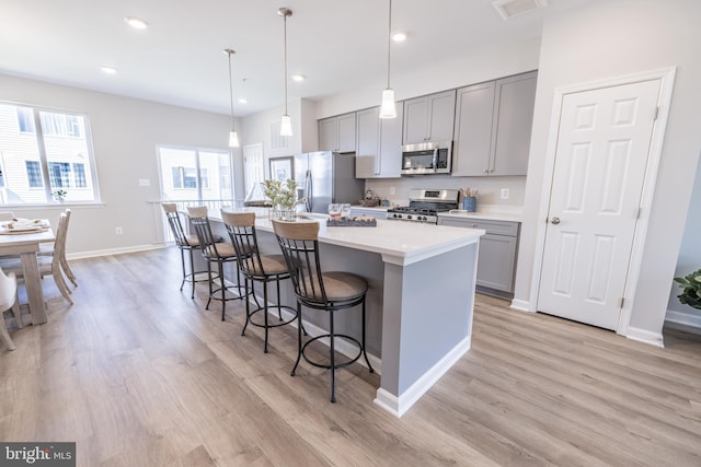 kitchen with light hardwood / wood-style flooring, gray cabinetry, stainless steel appliances, a center island with sink, and pendant lighting