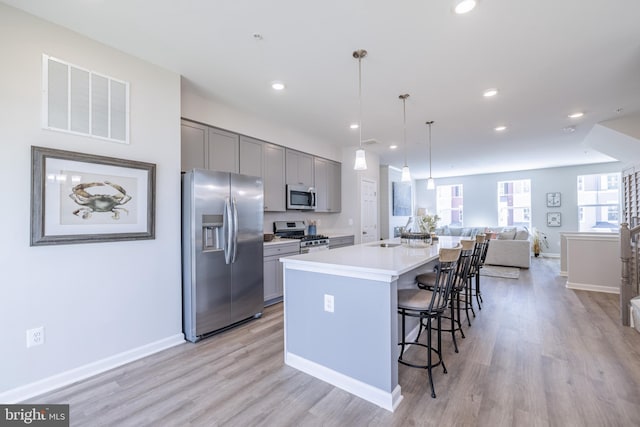 kitchen featuring gray cabinetry, pendant lighting, appliances with stainless steel finishes, and an island with sink