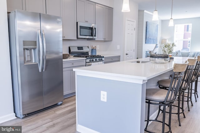 kitchen featuring an island with sink, stainless steel appliances, a kitchen bar, gray cabinets, and light hardwood / wood-style floors