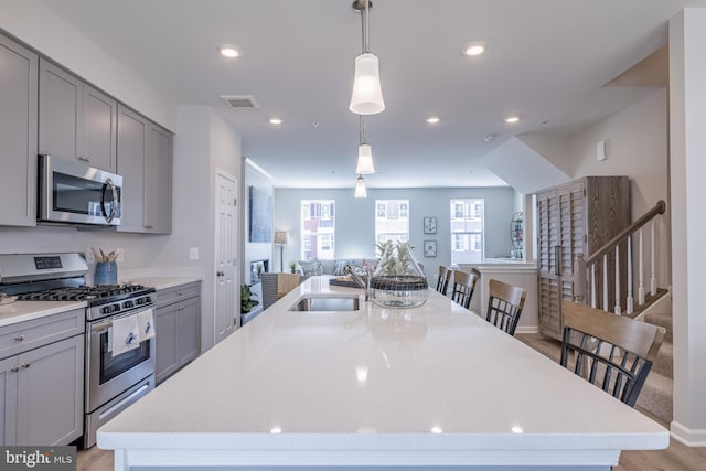 kitchen featuring appliances with stainless steel finishes, sink, light wood-type flooring, an island with sink, and pendant lighting