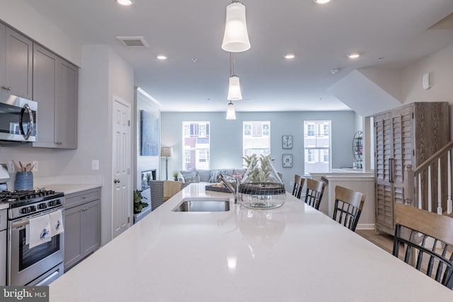 kitchen with appliances with stainless steel finishes, sink, pendant lighting, gray cabinets, and a breakfast bar area