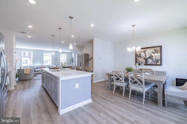 kitchen with an island with sink, light wood-type flooring, pendant lighting, gray cabinets, and sink