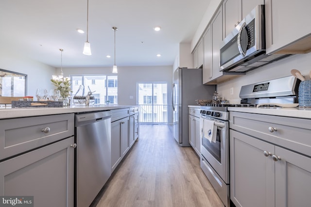 kitchen with appliances with stainless steel finishes, light hardwood / wood-style flooring, decorative light fixtures, and gray cabinets