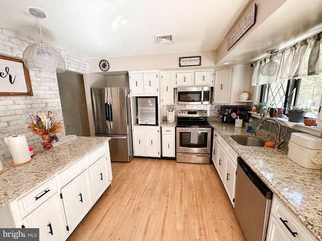 kitchen with hanging light fixtures, sink, white cabinetry, appliances with stainless steel finishes, and light wood-type flooring