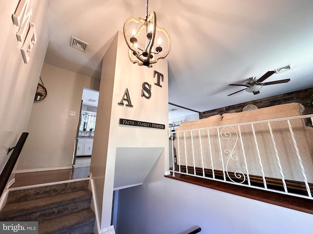 stairway featuring ceiling fan with notable chandelier