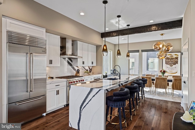 kitchen with wall chimney exhaust hood, beam ceiling, high end appliances, dark hardwood / wood-style floors, and an island with sink