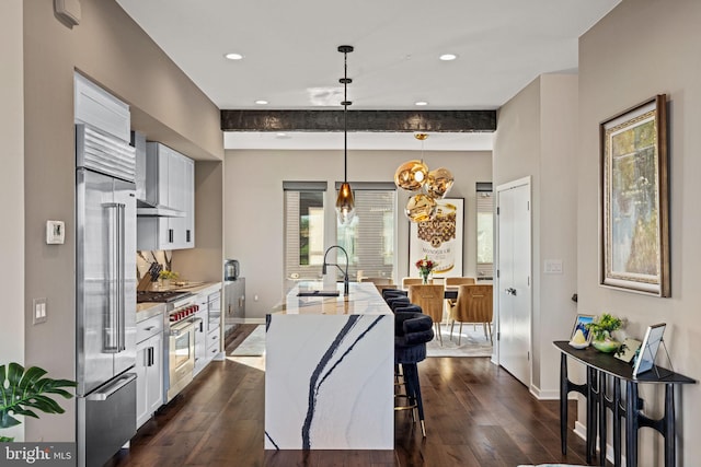 kitchen featuring high quality appliances, a center island with sink, decorative light fixtures, dark hardwood / wood-style floors, and white cabinets