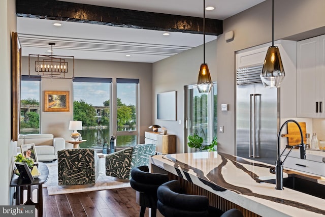 dining area with dark wood-type flooring, a notable chandelier, beamed ceiling, and sink