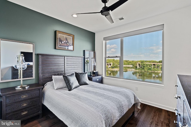 bedroom featuring dark wood-type flooring, a water view, and ceiling fan