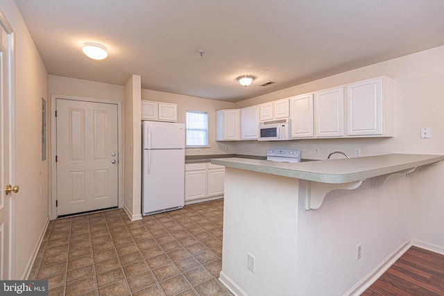 kitchen with a breakfast bar area, kitchen peninsula, white cabinets, and white appliances