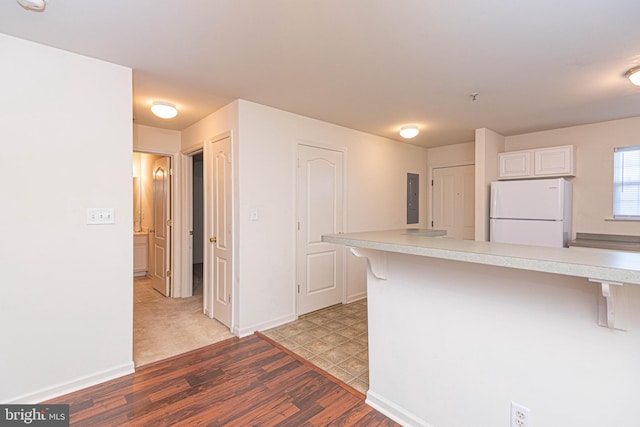 kitchen featuring white cabinets, electric panel, hardwood / wood-style flooring, a kitchen bar, and white refrigerator