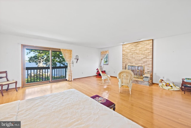 bedroom featuring a brick fireplace, hardwood / wood-style flooring, and access to outside