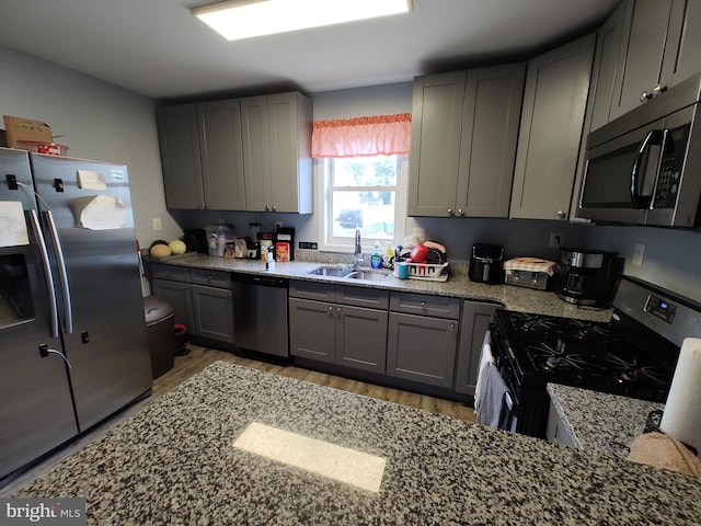 kitchen with stainless steel appliances, sink, gray cabinets, light stone countertops, and light wood-type flooring