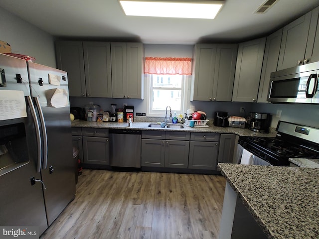 kitchen with gray cabinetry, light stone counters, appliances with stainless steel finishes, sink, and light hardwood / wood-style floors