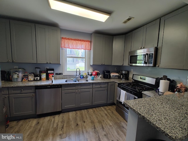 kitchen with light hardwood / wood-style floors, light stone counters, sink, gray cabinetry, and appliances with stainless steel finishes