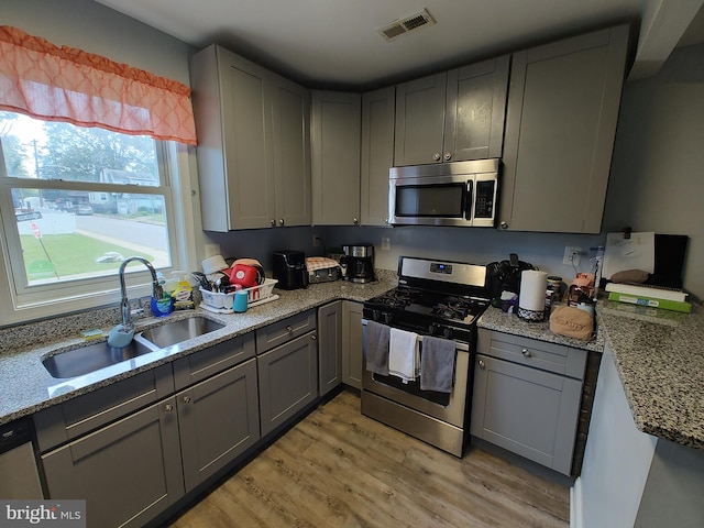 kitchen with stainless steel appliances, light stone counters, sink, gray cabinets, and light hardwood / wood-style flooring