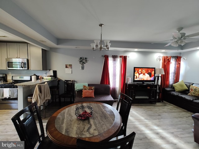 dining space with ceiling fan with notable chandelier and light wood-type flooring