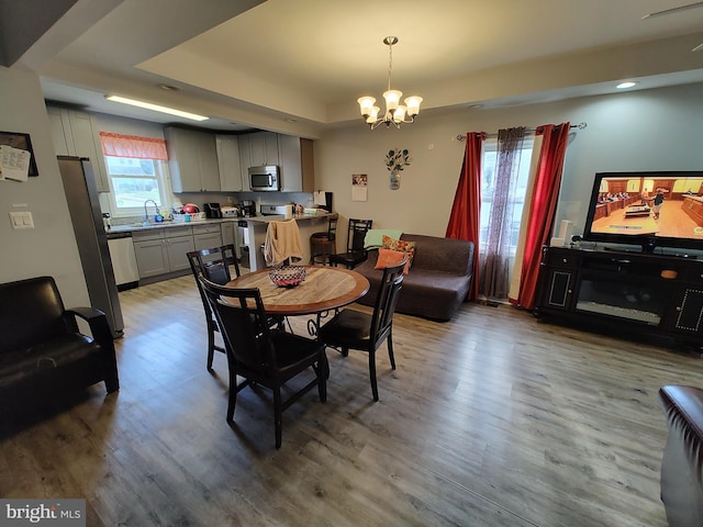 dining room featuring a raised ceiling, sink, hardwood / wood-style flooring, and a notable chandelier