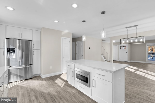 kitchen featuring a center island, hanging light fixtures, stainless steel appliances, white cabinetry, and wood-type flooring